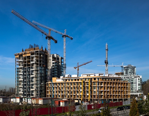 New construction of high-rise buildings in Burnaby city, industrial construction site, construction equipment, several construction cranes   on the background of finished skyscrapers and a clean blue sky